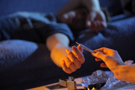 Close up of a young man who gives a joint to his friend lying on the couchの写真素材