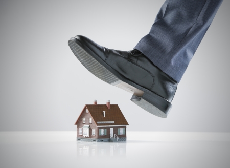 Businessman foot about to crush a small houseの写真素材