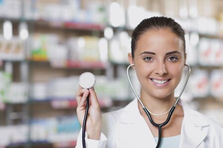 Young woman doctor holding stethoscope in pharmacyの写真素材