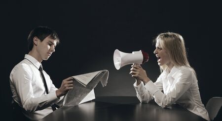Girl with megaphone, shouting loudly, young man is reading a newspaper ignoring herの写真素材