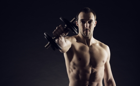 Muscular male athlete is training by lifting dumbbellsの写真素材