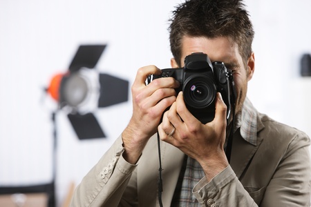 Young man taking photo with professional digital camera, focus on hand and lensの写真素材