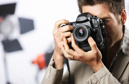 Young man taking photo with professional digital camera, focus on hand and lensの写真素材