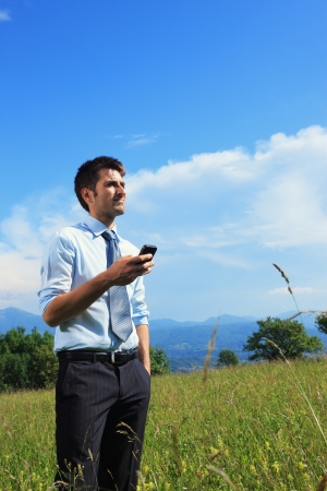 Businessman using smart phone in the meadow on a sunny dayの写真素材