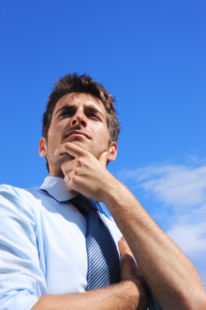Young business man looking up against a blue skyの写真素材