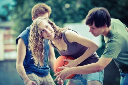 Two boys and a girl playing a game of basketball on an outdoor court.の写真素材