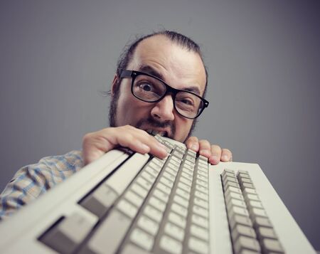 Eccentric angry man bites a keyboardの写真素材