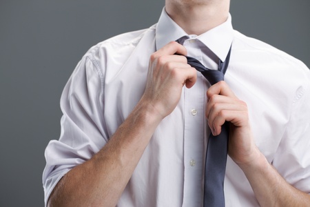Young business man taking off tie on grey background の写真素材