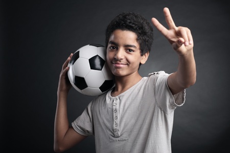 Portrait of young boy with a soccer ball signing victoryの写真素材