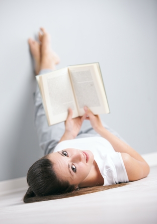 Portrait of a cute young female laying by the wall reading a bookの写真素材