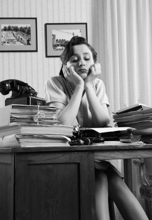 A bored office worker sitting behind a large stack of paperworkの写真素材