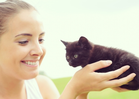 Beautiful young woman playing outdoors with her kittyの写真素材