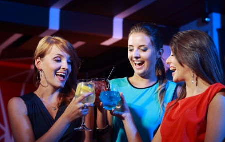 Group of happy beautiful young female friends celebrating in a nightclub with glasses of cocktail in...
