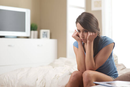 Portrait of young sad woman sitting on bedの写真素材