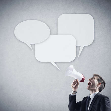 Angry young businessman shouting into megaphone against grey background の写真素材