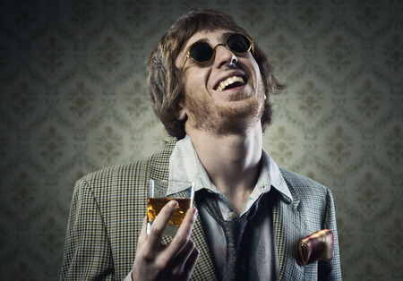 Funny guy holding a glass of whisky and posing against vintage wallpaper.の写真素材