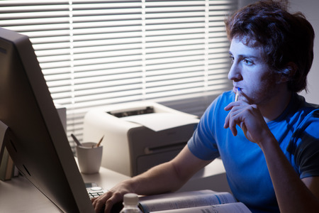 Young man staring at computer and holding a pen with office on background.の写真素材