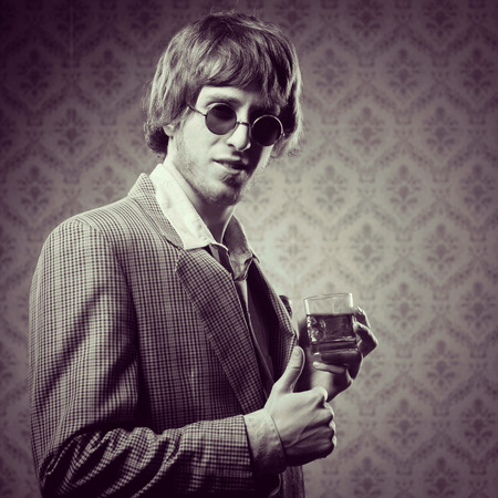 Funny guy holding a glass of whisky and posing against vintage wallpaper.の写真素材