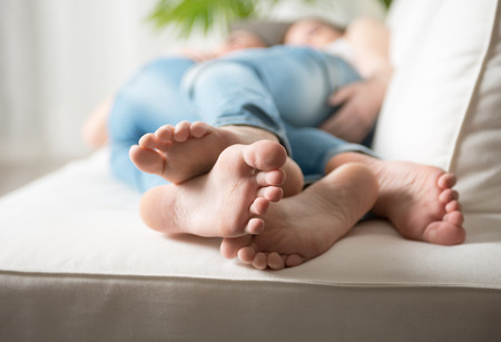 Loving young lesbian couple embracing on sofa, feet close-up.