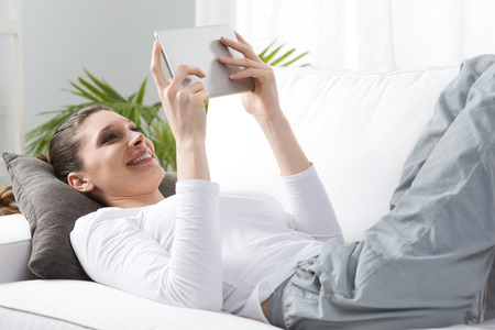 Smiling woman relaxing in the living room using digital tablet.の写真素材