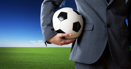 Businessman holding a soccer ball with blue sky and green meadow on background.の写真素材