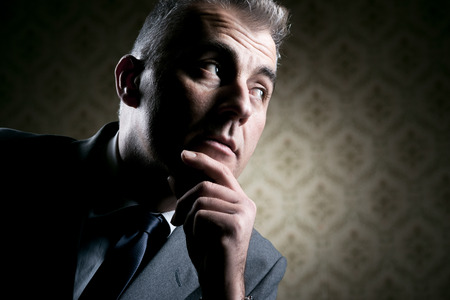 Vintage businessman with pensive expression on retro wallpaper background.の写真素材