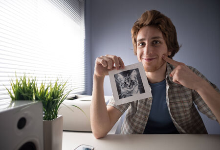Young guy smiling at camera and showing a cat's picture.の写真素材