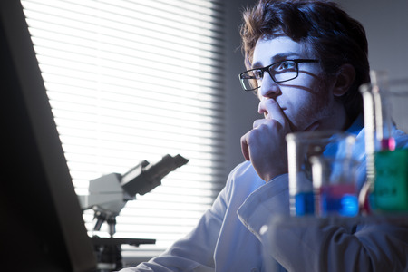 Researcher working at computer in the laboratory with hand on chin.の写真素材