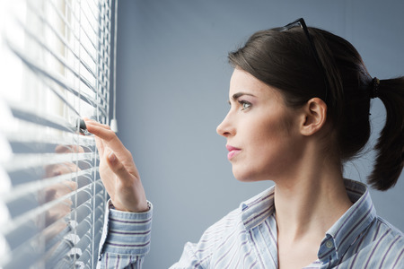 Young attractive woman peeking through blinds at window.の写真素材