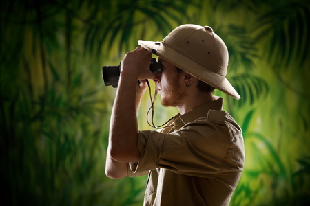 Young confident explorer in the rainforest jungle looking through binoculars.の写真素材