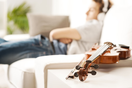 Violin close-up with man relaxing and listening to music on background.の写真素材