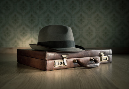 Borsalino hat on leather vintage briefcase on wooden surface with vintage wallpaper on background.の写真素材