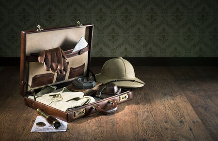 Colonial style explorer packing with open leather briefcase, pith hat, leather gloves, maps and brass telescope.の写真素材