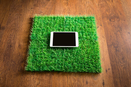 Blank ipad on squared artifical grass tile lying on hardwood floor.の写真素材