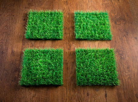 Four artificial turf tiles on hardwood floor, environmental care concept.の写真素材