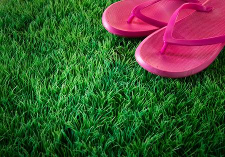Pink flip flops on green lush artificial grass, summer and vacations concept.の写真素材