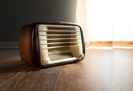 Vintage radio next to a window with curtain on hardwood floor.の写真素材