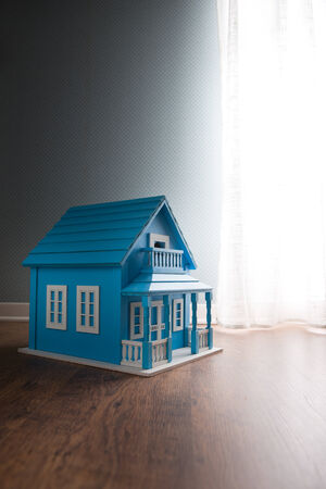 Blue wooden model house next to a window with curtain on wooden floor.の写真素材