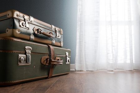 Pile of vintage suitcases next to a window on hardwood floor.の写真素材