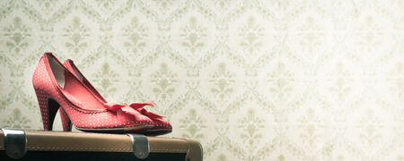 Glamour red dotted shoes on a vintage suitcase, retro wallpaper on background.の写真素材