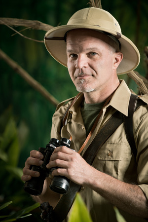 Smiling explorer in colonial style clothing holding binoculars and looking at camera.