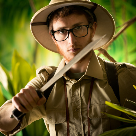 Watchful young adventurer holding a machete walking through the jungle.の写真素材