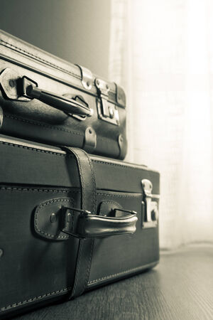 Pile of vintage suitcases next to a window on hardwood floor.の写真素材