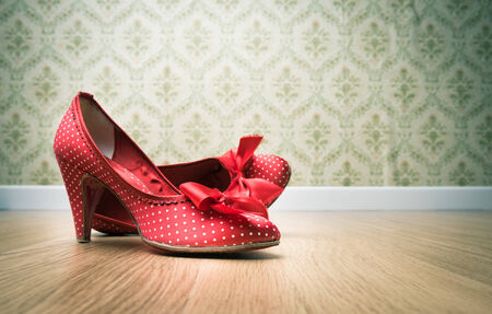 Vintage red dotted female shoes with ribbon on hardwood floor with retro wallpaper on background.の写真素材