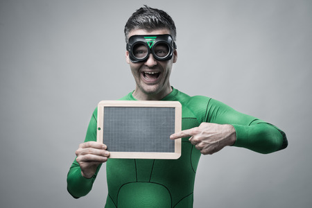 Cheerful green superhero pointing to an empty blackboard.の写真素材