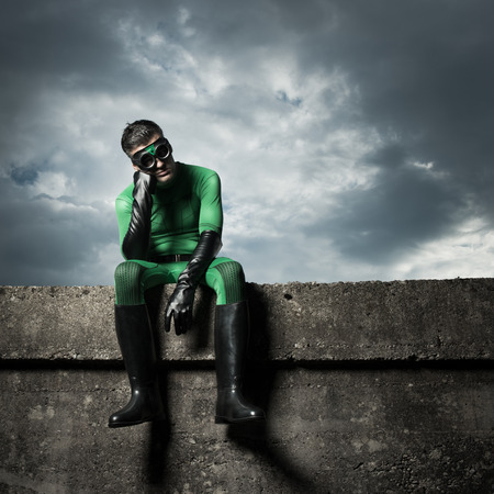 Pensive green superhero with hand on chin and cloudy dramatic sky on background.の写真素材