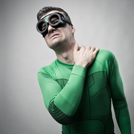 Green superhero touching his neck and shoulder and feeling pain.の写真素材