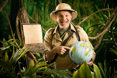Cheerful explorer in the jungle pointing to a globe next to a wooden sign.の写真素材