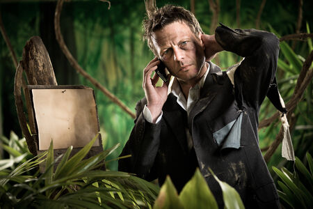 Lost businessman in the jungle with mobile phone and empty sign.の写真素材