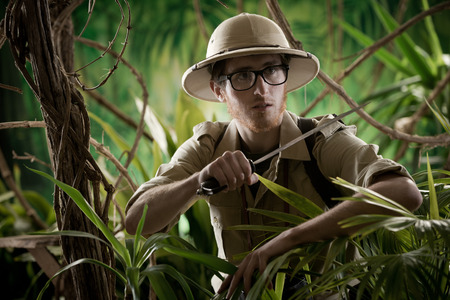 Watchful young adventurer holding a machete walking through the jungle.の写真素材